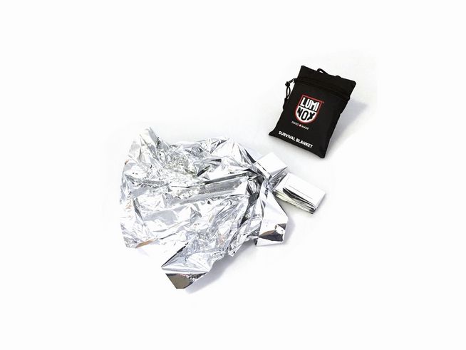 Die Luminox Survival Decke in silberner Farbe liegt zusammengefaltet auf weißem Hintergrund, neben ihr befindet sich die schwarze Verpackung mit Luminox Logo und der Bezeichnung Survival Blanket.