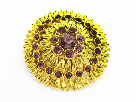 Runde lila Strass Brosche im Sexy City Look von Juwelier Harnisch, umgeben von goldfarbener Verzierung, farbenfrohes Design, ideal für besondere Anlässe.