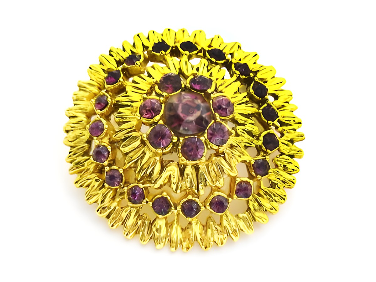 Runde lila Strass Brosche im Sexy City Look von Juwelier Harnisch, umgeben von goldfarbener Verzierung, farbenfrohes Design, ideal für besondere Anlässe.