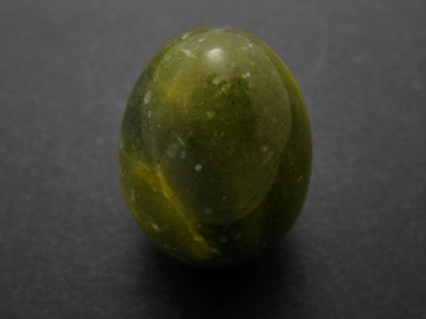 Ein dunkles grünlich-gelbes Stein-Ei aus Achat, naturbelassen und mit einer glatten Oberfläche, Maße 30 x 22 x 22 mm, gefertigt von Juwelier Harnisch.