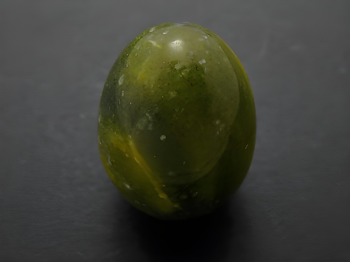 Ein dunkles grünlich-gelbes Stein-Ei aus Achat, naturbelassen und mit einer glatten Oberfläche, Maße 30 x 22 x 22 mm, gefertigt von Juwelier Harnisch.