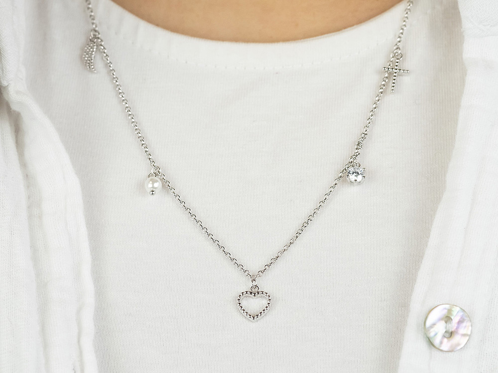 Silberne Kette von Engelsrufer mit Anhängern in Form eines Herzens, eines Kreuzes und einer Perle, verziert mit Zirkonia, getragen über einem weißen Oberteil.