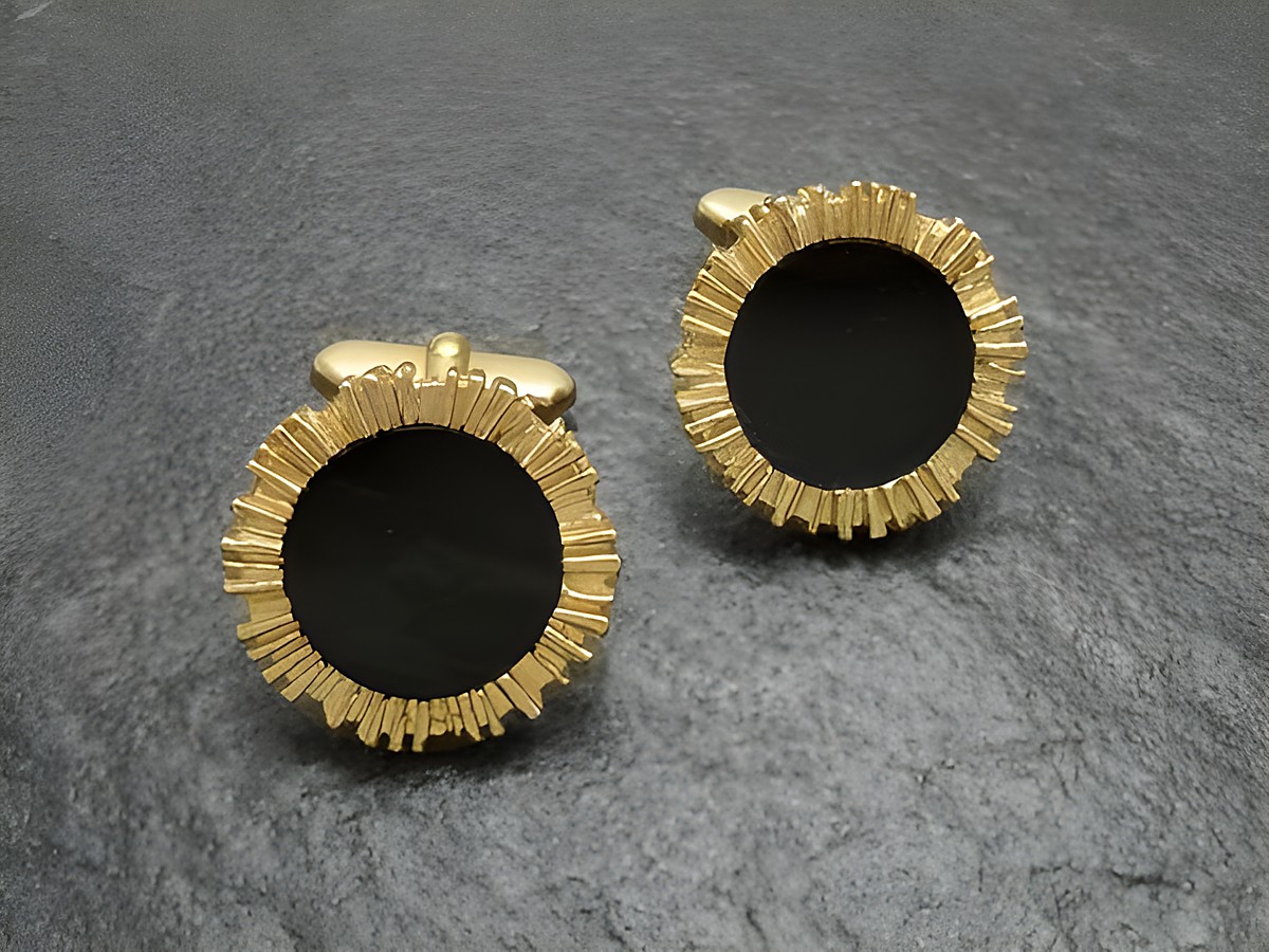 Vergoldete Manschettenknöpfe mit schwarzem Onyx-Look, umrandet von einer goldfarbenen Struktur, Hersteller Juwelier Harnisch, elegant und stilvoll für besondere Anlässe.