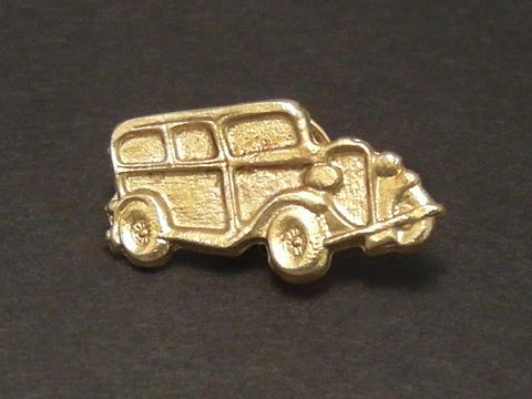Ein goldfarbener Pin in Form eines Oldtimer Autos mit detaillierten Konturen, hergestellt von Juwelier Harnisch, geeignet als Anstecknadel für Auto-Enthusiasten.