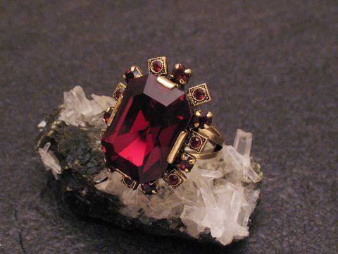 Modeschmuck Ring mit Granat Imitation in der Mitte, umgeben von Strasssteinen, auf einem unstrukturierten Untergrund aus Kristallen, Hersteller Juwelier Harnisch, City Ringe.