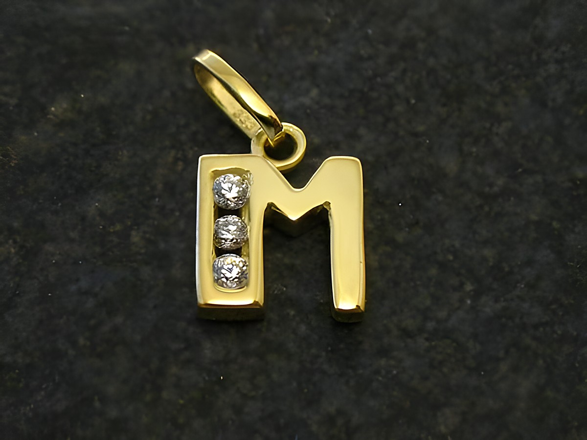 Goldener Anhänger mit dem Buchstaben M, verziert mit Zirkonia, Hersteller Juwelier Harnisch. Elegantes und stilvolles Design, ideal als persönliches Geschenk oder Schmuckstück.
