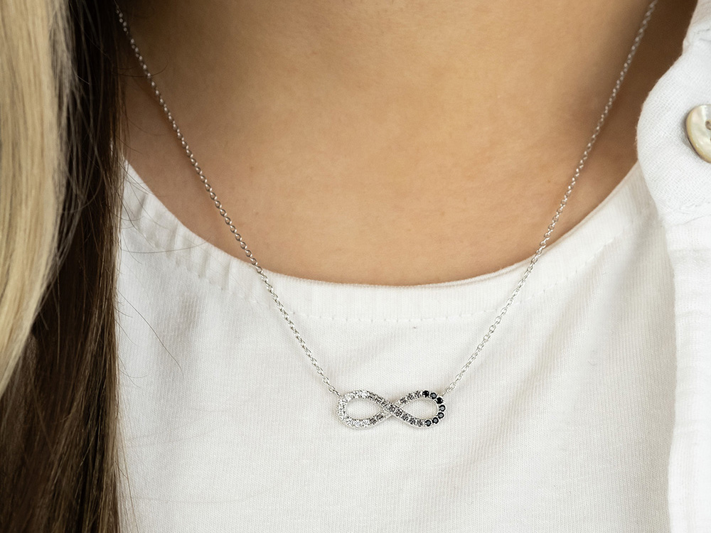 Die Kette zeigt ein silbernes Unendlichkeitssymbol mit Zirkonia, elegant getragen um den Hals einer Person, die ein weißes Oberteil trägt.