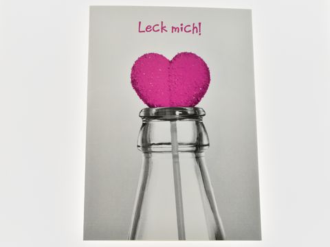 Eine Geburtstagskarte mit einem pinken Herzlolli in einer Flasche, darauf steht der Text Leck mich. Hersteller ist Juwelier Harnisch.