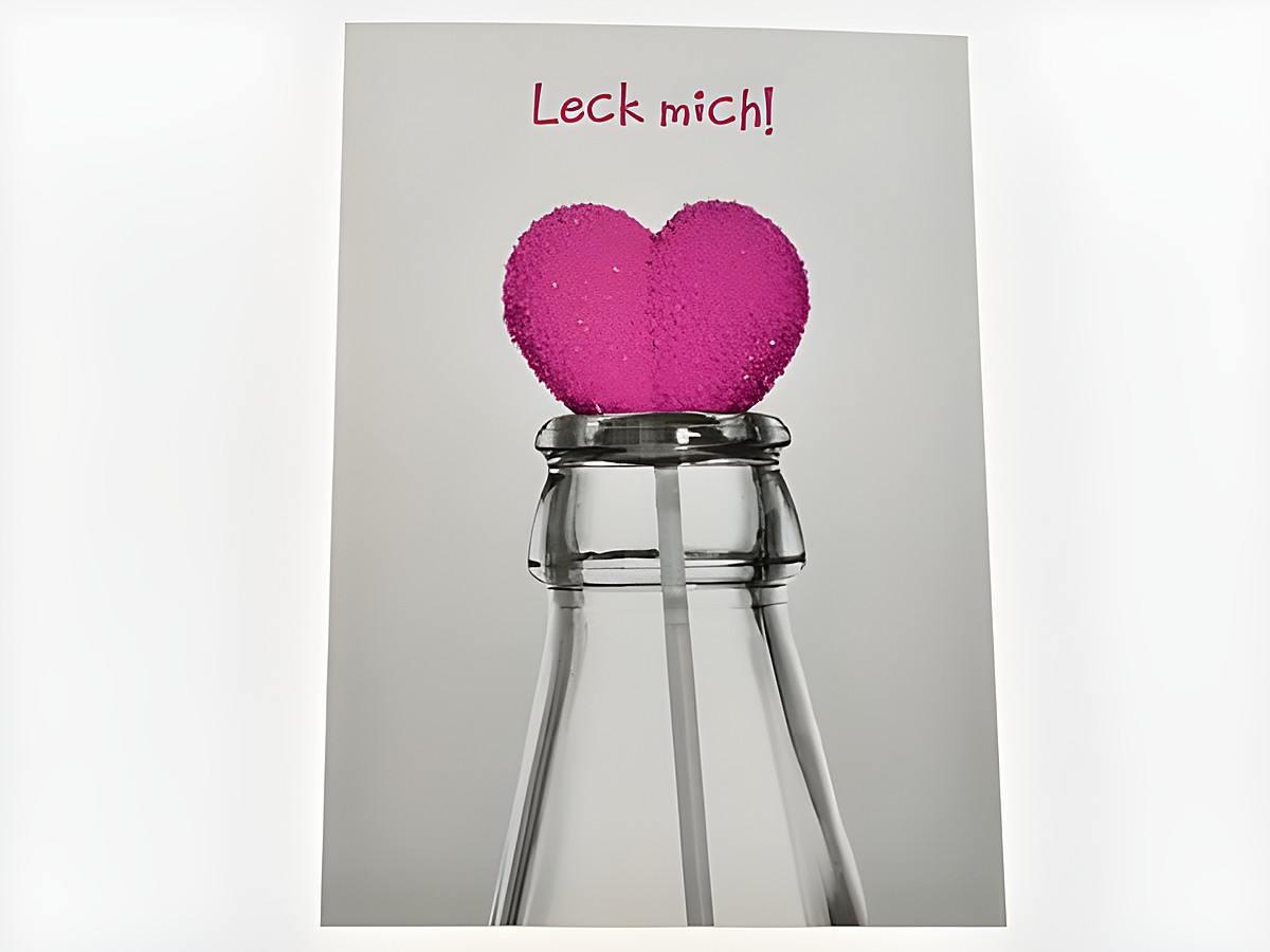 Eine Geburtstagskarte mit einem pinken Herzlolli in einer Flasche, darauf steht der Text Leck mich. Hersteller ist Juwelier Harnisch.
