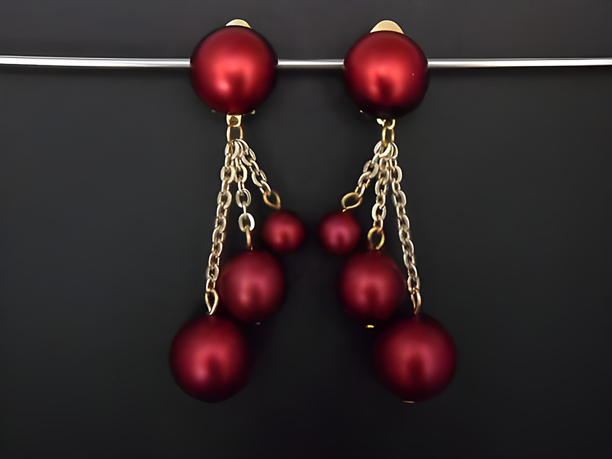 Weinrote Ohrclips mit goldfarbenen Elementen aus Kunstharz, zeitloses Design, ausgestattet mit Zierelementen in verschiedenen Größen und längeren Kettenanhängern, gleichzeitig elegant und auffällig.