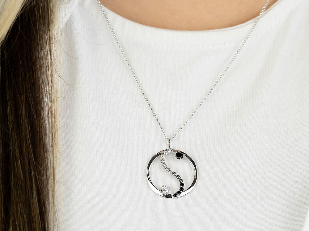 Eine silberne Kette mit Yin Yang Anhänger, verziert mit Zirkonia in Schwarz und Weiß, getragen von einer Person mit langen, glatten Haaren und einem weißen Oberteil.