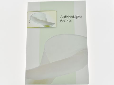 Trauerkarte mit Umschlag, auf der eine weiße Blüte abgebildet ist. Die Karte trägt die Aufschrift Aufrichtiges Beileid und stammt vom Hersteller Juwelier Harnisch.