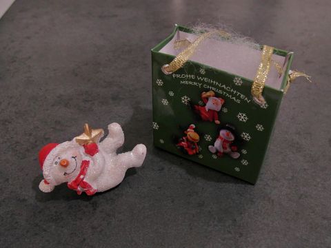 Ein liegender Schneemann mit Geschenktasche und einem Stern, Hersteller Juwelier Harnisch, gestaltet für Weihnachten, dekorativ und festlich.