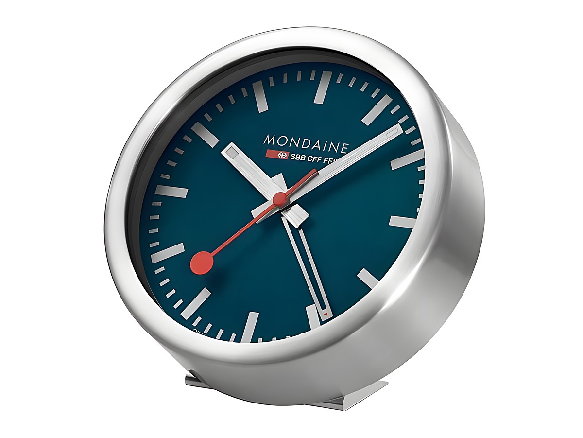 Wecker von Mondaine in Ozean Blau mit mattem Aluminiumgehäuse, Durchmesser 12,5 cm, zeigt klare Ziffern und rote Zeiger, ideal für moderne Tischgestaltung.