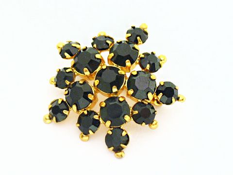 Strass Brosche in Schwarz, rundlich gefasst, aus dem Haus Juwelier Harnisch. Die Brosche glänzt mit schwarzen Strasssteinen, die in goldfarbenen Fassungen arrangiert sind.