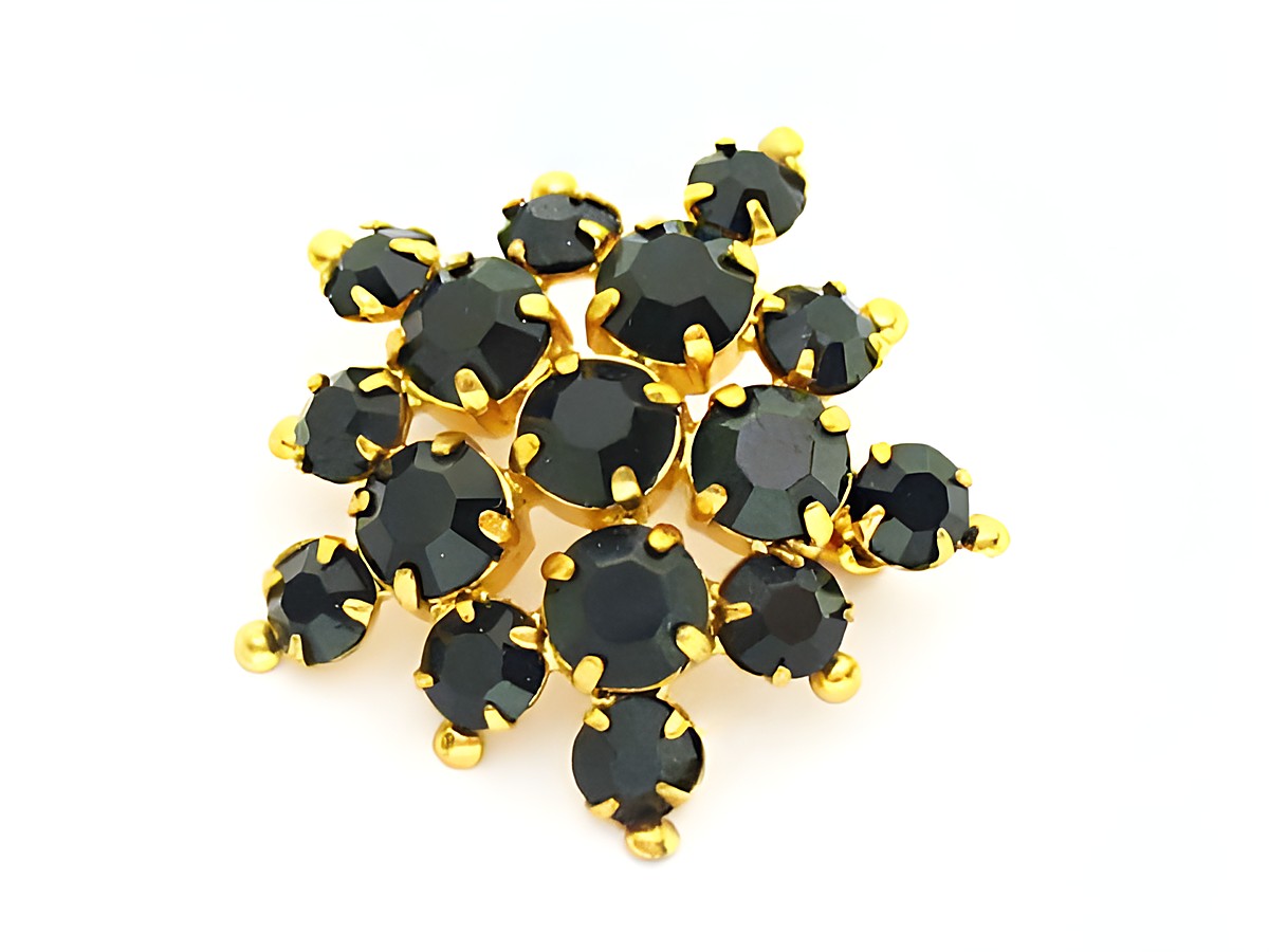 Strass Brosche in Schwarz, rundlich gefasst, aus dem Haus Juwelier Harnisch. Die Brosche glänzt mit schwarzen Strasssteinen, die in goldfarbenen Fassungen arrangiert sind.