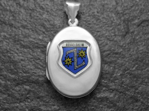 Das Bild zeigt ein silbernes Medaillon mit dem Wappen von Rüsselheim, das in Blau und Gelb gestaltet ist. Der Hersteller des Medaillons ist Juwelier Harnisch aus Hessen.