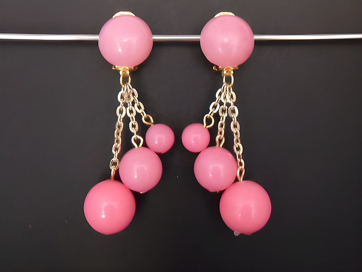 Ohrclip in rosa zeitlos mit goldfarbenen Akzenten und Kunstharzkugeln, hergestellt von Juwelier Harnisch, präsentiert ein auffälliges Design mit hängenden Elementen.