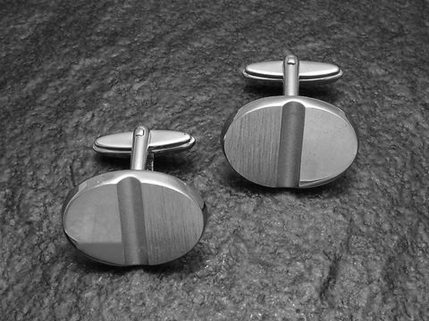 Manschettenknöpfe Silber im Modell Digital-Cut von Juwelier Harnisch aus echtem Silber, elegant und modern mit strukturiertem Design in ovaler Form, auf einem dunklen Untergrund platziert.