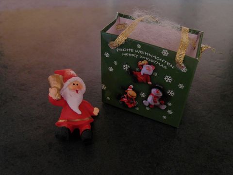 Weihnachtsmann mit Geschenktasche sitzend neben einer dekorativen Geschenkschachtel von Juwelier Harnisch, ideal für die Weihnachtszeit.
