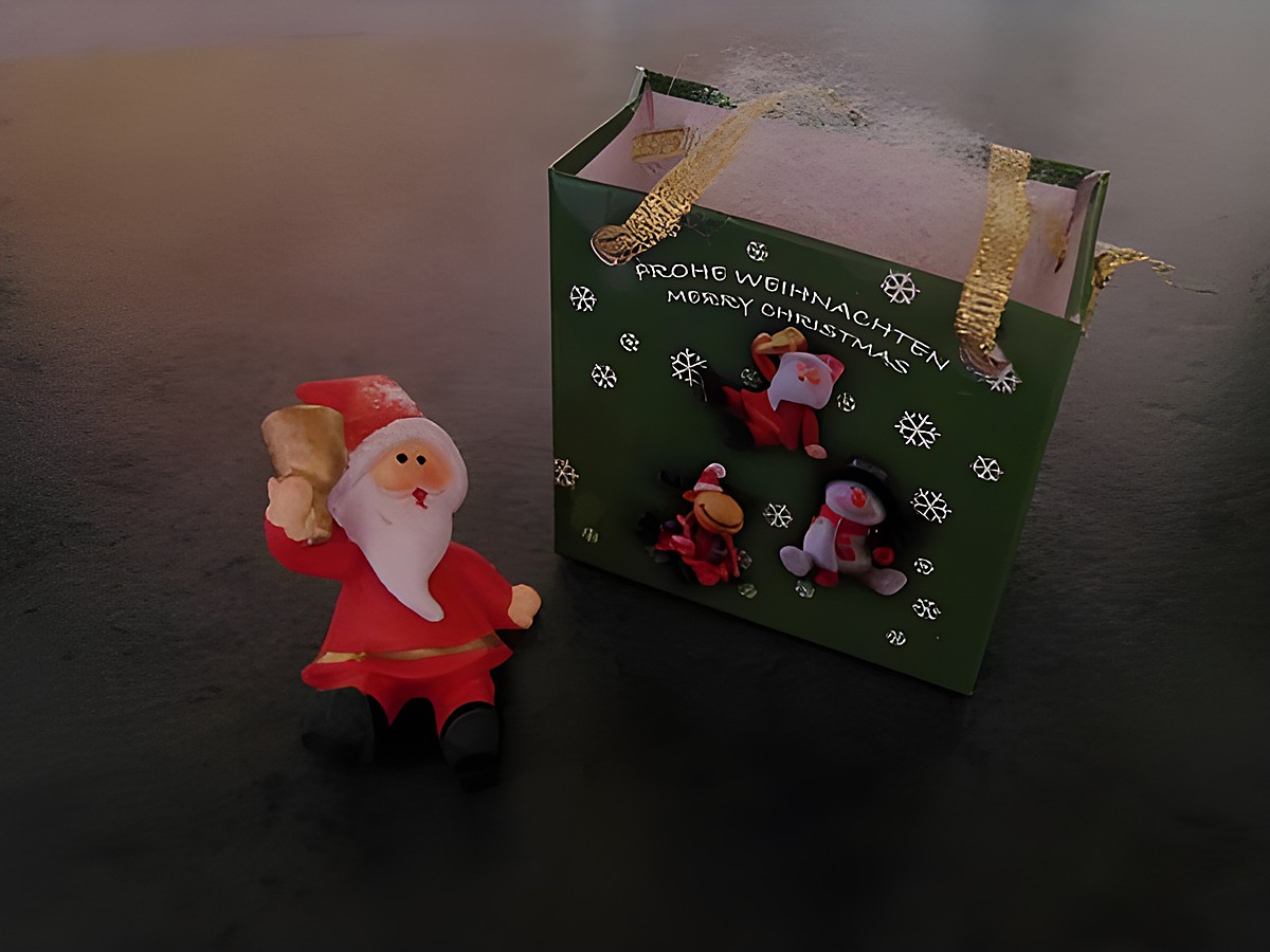 Weihnachtsmann mit Geschenktasche sitzend neben einer dekorativen Geschenkschachtel von Juwelier Harnisch, ideal für die Weihnachtszeit.