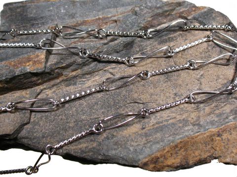 Lange Silberkette mit Elementen rhodiniert DESIGN, Hersteller: Juwelier Harnisch, Mittelteil Colliers, dekorativ auf einem steinernen Untergrund präsentiert.