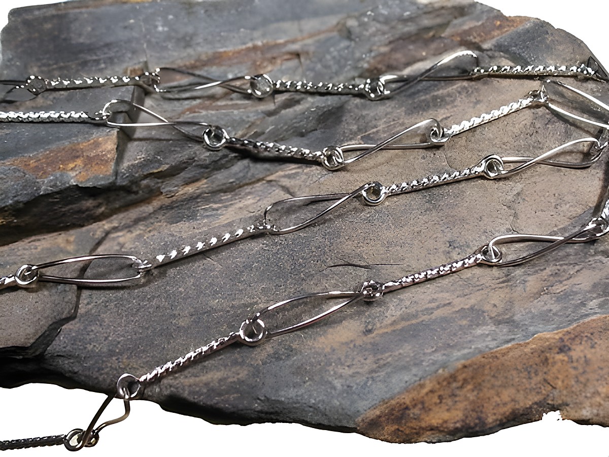 Lange Silberkette mit Elementen rhodiniert DESIGN, Hersteller: Juwelier Harnisch, Mittelteil Colliers, dekorativ auf einem steinernen Untergrund präsentiert.