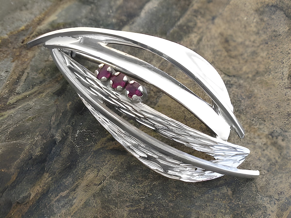 Brosche im Design mit Rubin aus Sterling Silber rhodiniert, von Juwelier Harnisch, mit eleganten geschwungenen Formen und drei rubinroten Steinen. Ideal für stilvolle Akzente.