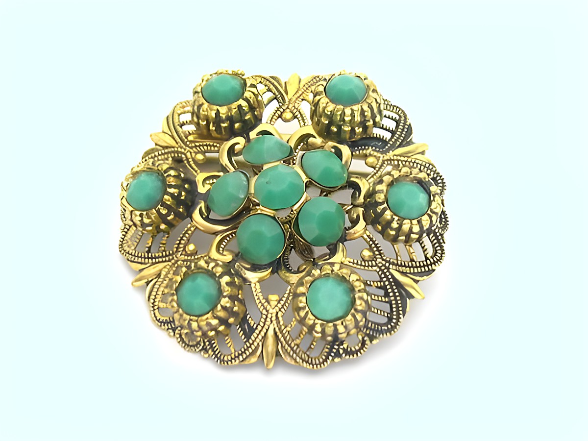 Brosche im Sexy City Look in smaragdgrün, rund mit filigranem Goldrahmen und mehreren türkisfarbenen Steinen, Hersteller: Juwelier Harnisch.
