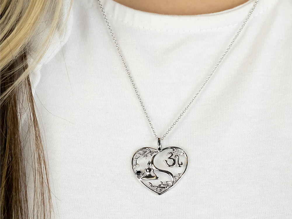 Eine silberne Kette mit einem herzförmigen Anhänger, der ein Yin Yang Symbol zeigt, umrahmt von floralen Mustern. Der Anhänger ist mit Zirkonia verziert und hat die Aufschrift Om.