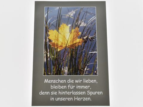 Eine Trauerkarte mit einem Bild eines gelben Blattes im Schilf, umgeben von Wasser. Darunter steht der Text, dass geliebte Menschen Spuren in unseren Herzen hinterlassen.
