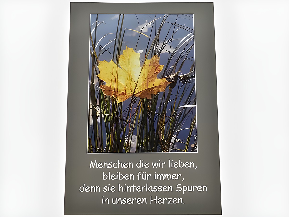 Eine Trauerkarte mit einem Bild eines gelben Blattes im Schilf, umgeben von Wasser. Darunter steht der Text, dass geliebte Menschen Spuren in unseren Herzen hinterlassen.