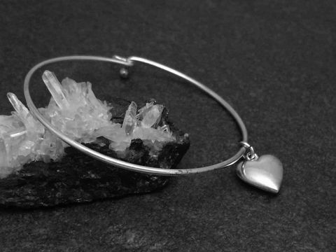 Silber Armreifen mit Herzanhänger, Durchmesser 17 cm und 1,6 mm dick, hergestellt vom Juwelier Harnisch, gelegen auf einem schwarzen Untergrund mit Kristallen.