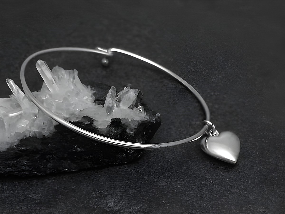 Silber Armreifen mit Herzanhänger, Durchmesser 17 cm und 1,6 mm dick, hergestellt vom Juwelier Harnisch, gelegen auf einem schwarzen Untergrund mit Kristallen.