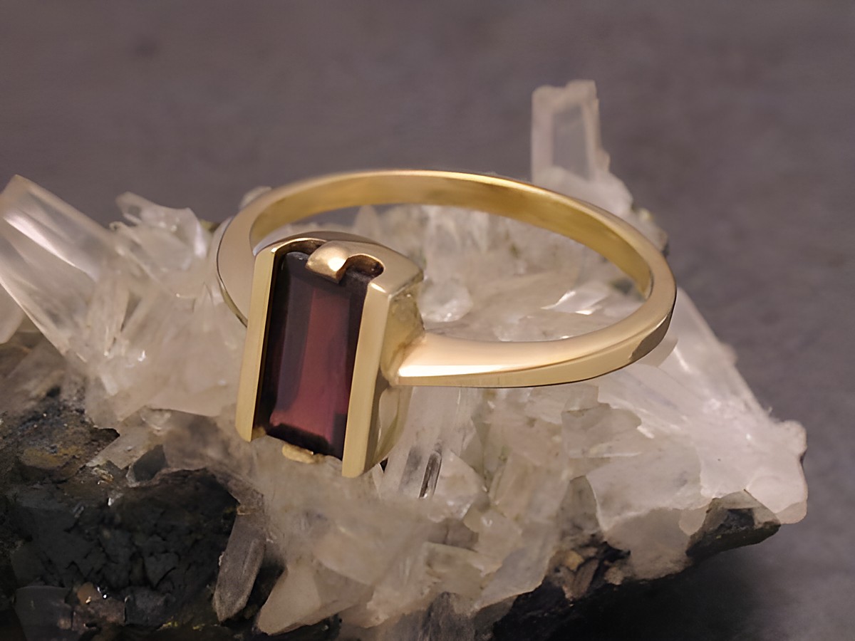 Ein puristischer Goldring aus Gold 333 mit einem rechteckigen Granat, Größe 53,5, vom Juwelier Harnisch, geeignet bis Größe 54/17,5, auf einem mineralischen Untergrund.