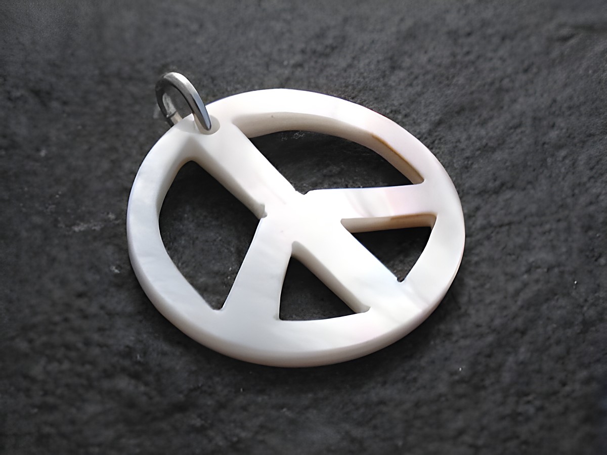 Ein Anhänger in Form eines Peacezeichens aus Perlmutt mit einer Sterlingsilberöse, hergestellt von Juwelier Harnisch. Der Anhänger hat eine glänzende, elegante Oberfläche.
