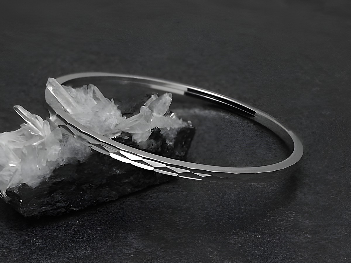 Silber Armreifen - zeitlos - 3 mm - rhodiniert - 18 cm vom Hersteller Juwelier Harnisch, schön präsentiert auf einer schwarzen Fläche mit Kristallen im Hintergrund.
