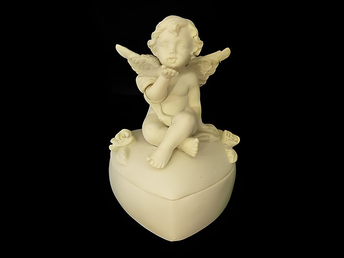 Eine Schutzengel Dose in Herzform mit einer sitzenden Schutzengel Figur. Der Engel hat Flügel und hält eine Hand zum Kuss. Ideal als Geschenkidee. Hersteller Juwelier Harnisch.