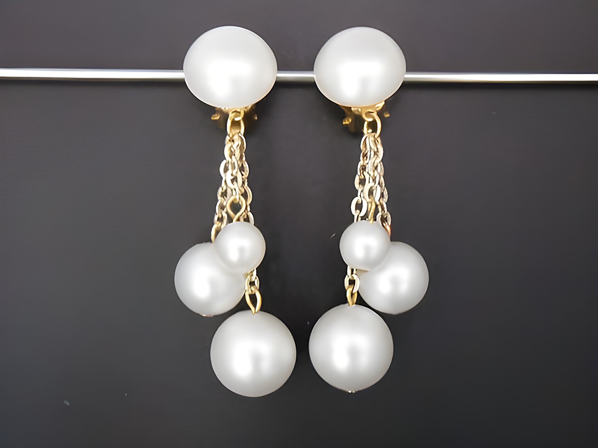 Zeitlose Ohrclips aus perlweißem Kunstharz und goldfarbenen Details, mit mehreren hängenden Perlen, Hersteller Juwelier Harnisch. Elegantes Accessoire für besondere Anlässe.