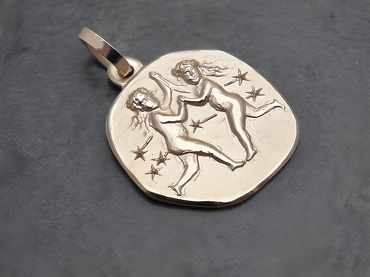Ein goldener Anhänger mit dem Sternzeichen Zwillinge, der zwei tanzende Figuren und Sterne zeigt, hergestellt vom Juwelier Harnisch, ideal für Liebhaber astrologischer Schmuckstücke.