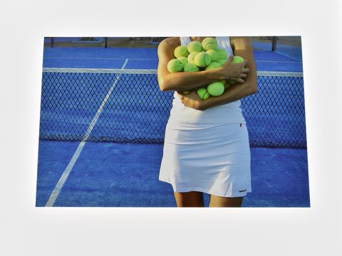 Tennisspielerin steht auf einem blauen Tenniscourt und hält viele gelbe Tennisbälle in den Armen. Hersteller der Grußkarte ist Juwelier Harnisch.