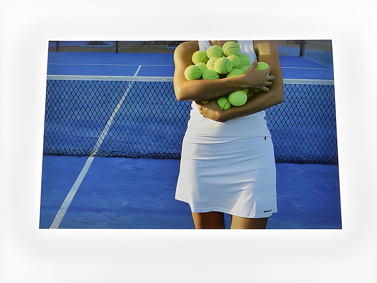 Tennisspielerin steht auf einem blauen Tenniscourt und hält viele gelbe Tennisbälle in den Armen. Hersteller der Grußkarte ist Juwelier Harnisch.