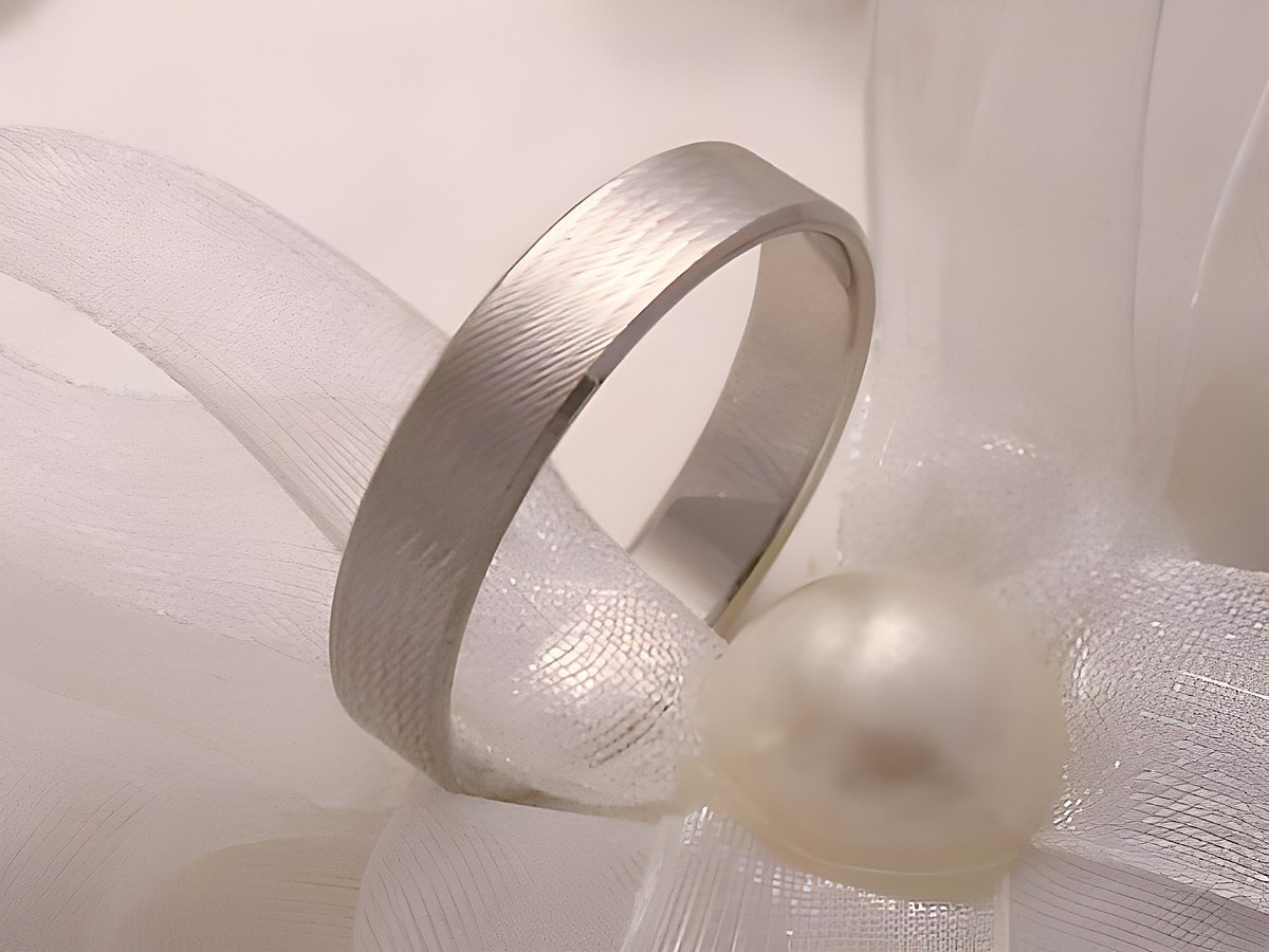 Trauring Ehering WHITE ELEGANCE aus 333 Weißgold, mit einer eleganten Oberfläche, abgebildet auf einem zarten Satinband und einer Perle, erhältlich bis Größe 56/17,8, Hersteller Juwelier Harnisch.