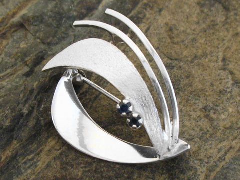Elegante Brosche aus Sterling Silber rhodiniert mit geschwungenem Design und Saphiren, hergestellt von Juwelier Harnisch, ideal für stilvolle Akzente in jedem Outfit.
