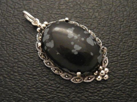 Schneeflocken-Obsidian Cabochon in einem filigranen Silbermedaillon Anhänger, elegant gestaltet mit geschwungenen Verzierungen und kleinen Details, ideal als Schmuckstück für besondere Anlässe.