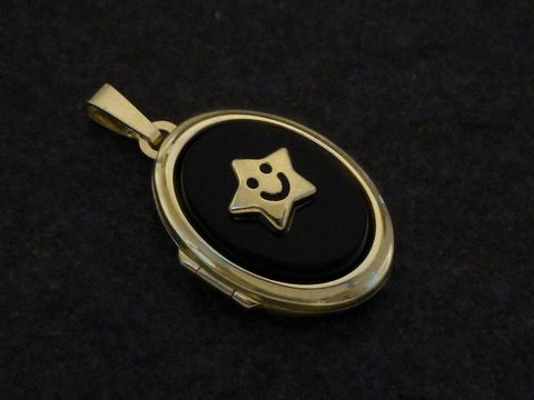 Ein ovales Medaillon aus Gold 333 mit einem schwarzen Cabochon und einem lächelnden Sternmotiv in der Mitte, hergestellt von Juwelier Harnisch. Ideal als Schmuckstück für besondere Anlässe.
