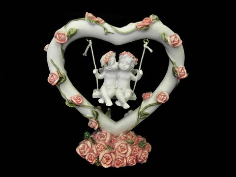Eine liebevoll gestaltete Schutzengel Figur in Herzform, die zwei engelliche Kinder auf einer Schaukel zeigt, umgeben von zarten Rosen. Hersteller Juwelier Harnisch.