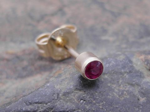 Ein goldener unisex Ohrstecker mit einem noblen Rubin, Hersteller Juwelier Harnisch, Einzelohrring, 1 Stück auf einer steinernen Unterlage.