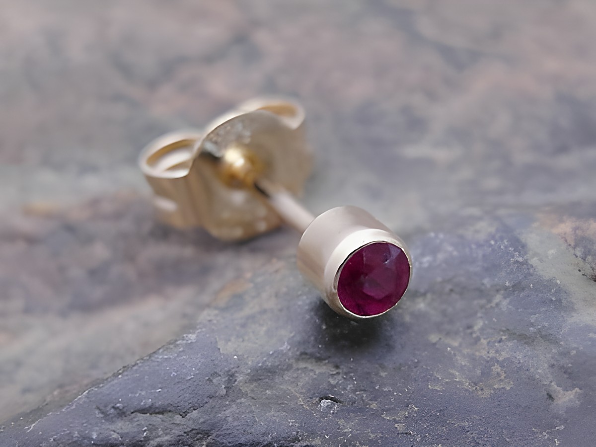 Ein goldener unisex Ohrstecker mit einem noblen Rubin, Hersteller Juwelier Harnisch, Einzelohrring, 1 Stück auf einer steinernen Unterlage.