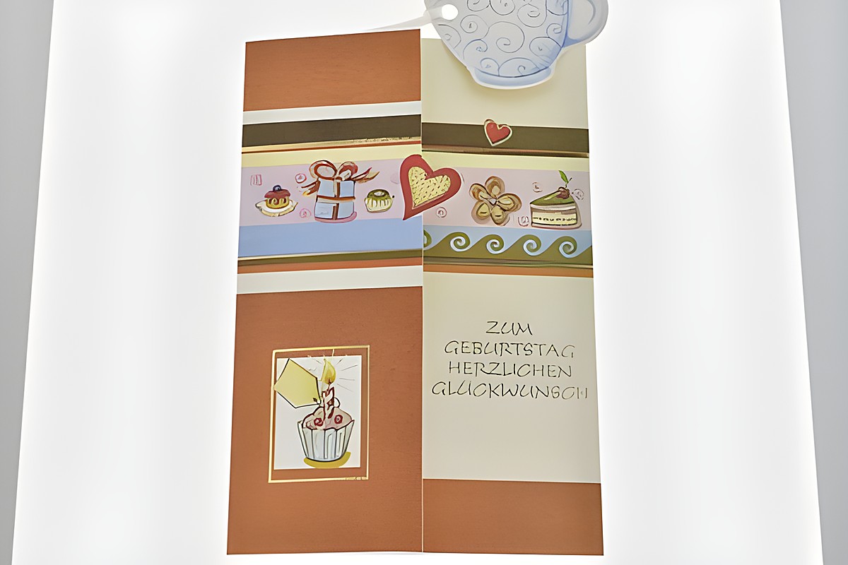 Eine Geburtstagskarte mit bunten Verzierungen, auf der ein Kuchen und kleine Törtchen abgebildet sind, samt dem Schriftzug "Zum Geburtstag herzlichen Glückwunsch", Hersteller Juwelier Harnisch. – Ansicht 2